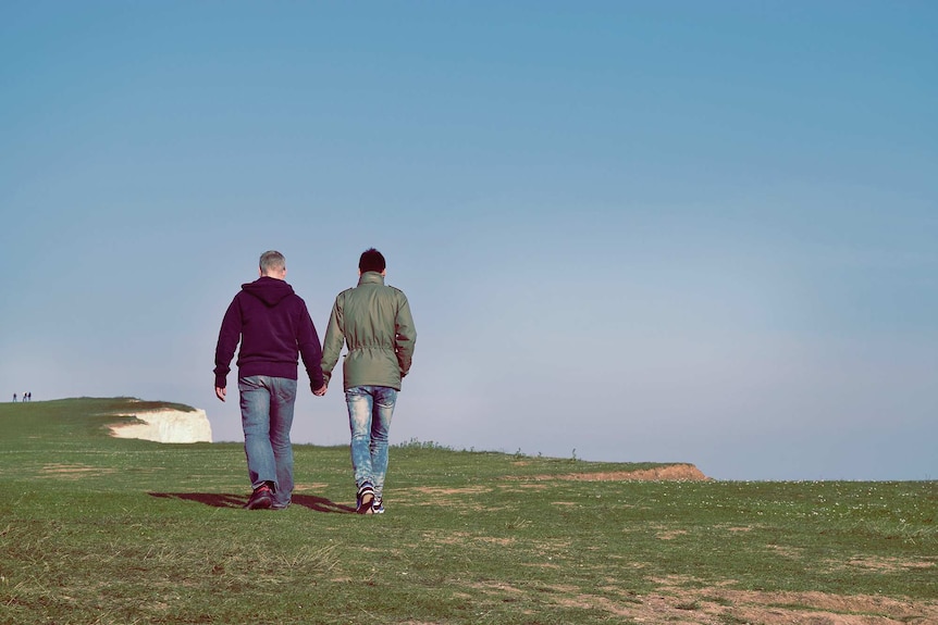 Two men holding hands and walking on a cliff away from the camera for a story about breaking up when the timing isn't right.