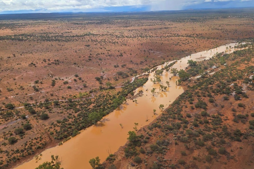 An aerial shot of a large stream of reddish-brown water in an outback landscape.