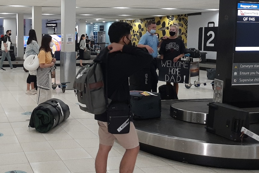 A young woman holds a sign saying, welcome home dad, at Perth Airport.