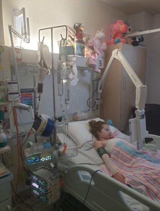 Brunette young girl lying in hospital bed surrounded by machines