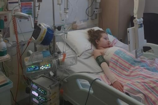 Brunette young girl lying in hospital bed surrounded by machines