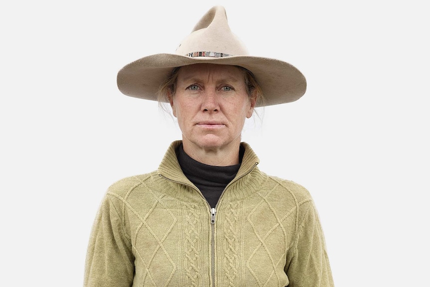 A woman wearing an Akubra-style hat and a mustard-coloured zip-up cardigan.