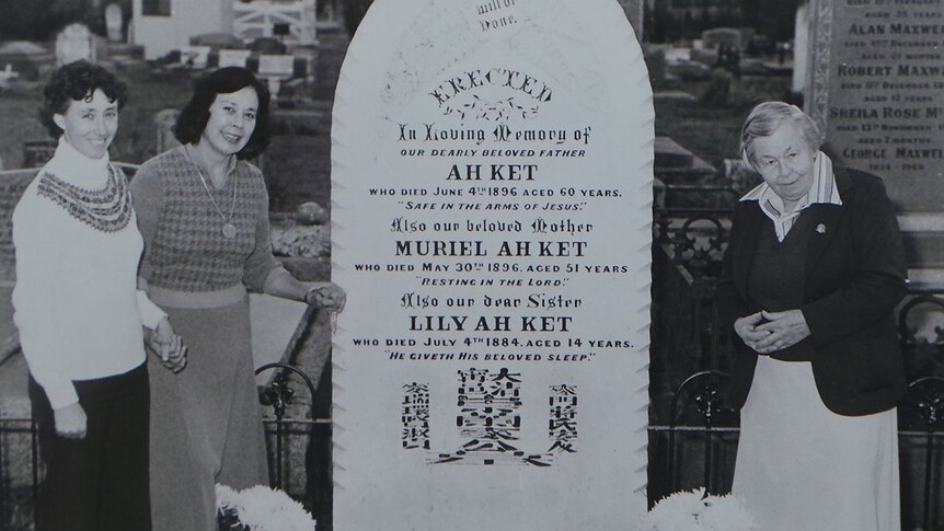 Black and white photo of relatives standing by a grave