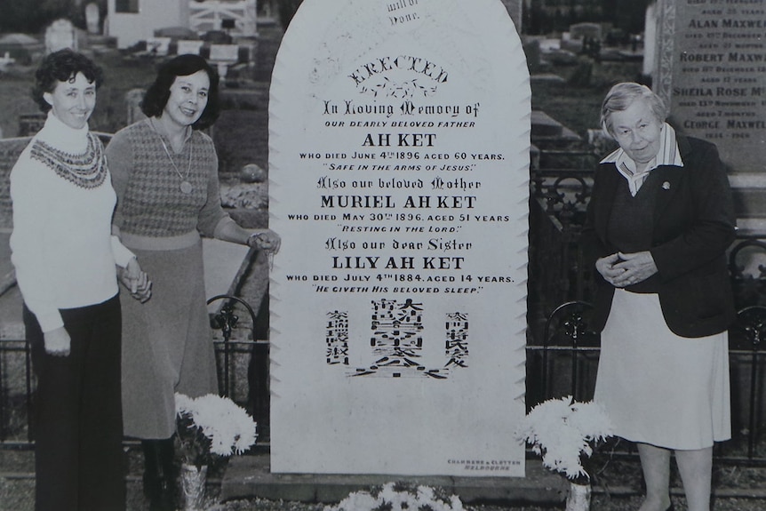 Black and white photo of relatives standing by a grave