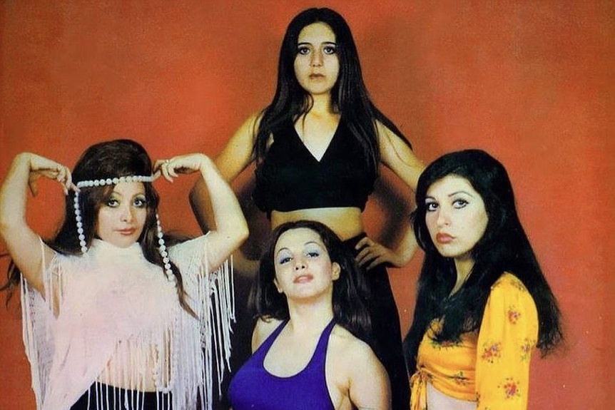 Four women in 1970s style clothing, against a red background.