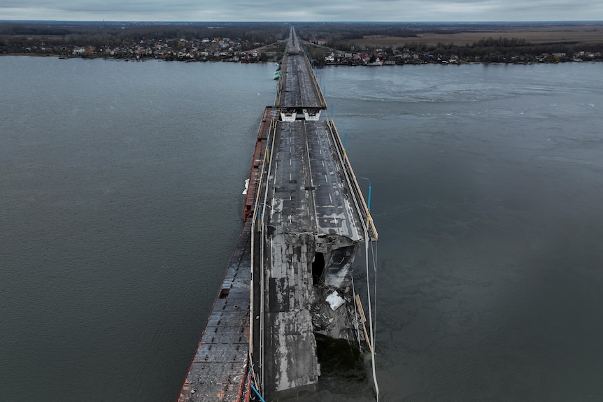 A view from over of the long bridge, with a section completely destroyed and falling into the water. 