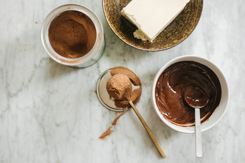 Three ingredients for chocolate malted mousse on a counter including Milo, melted chocolate and silken tofu.