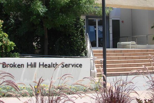 The words Broken Hill Health Service on a sign on a white concrete wall outside a building with steps at the entrance.