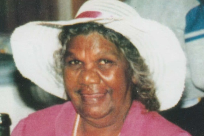 a photograph of an Aboriginal woman in a wide, white hat and a pink dress laughing