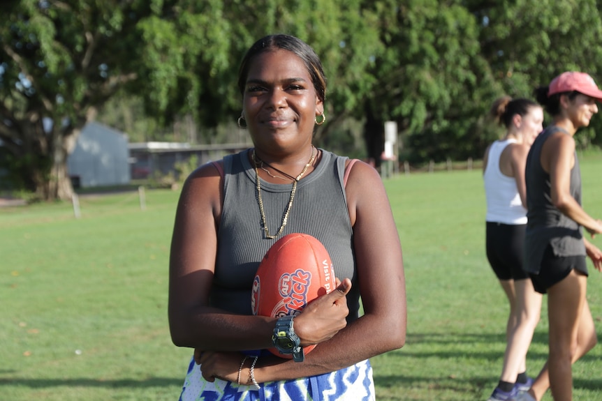 Whitney Yunupiŋu smiles and holds a red football at the Nhulunbuy footy oval.
