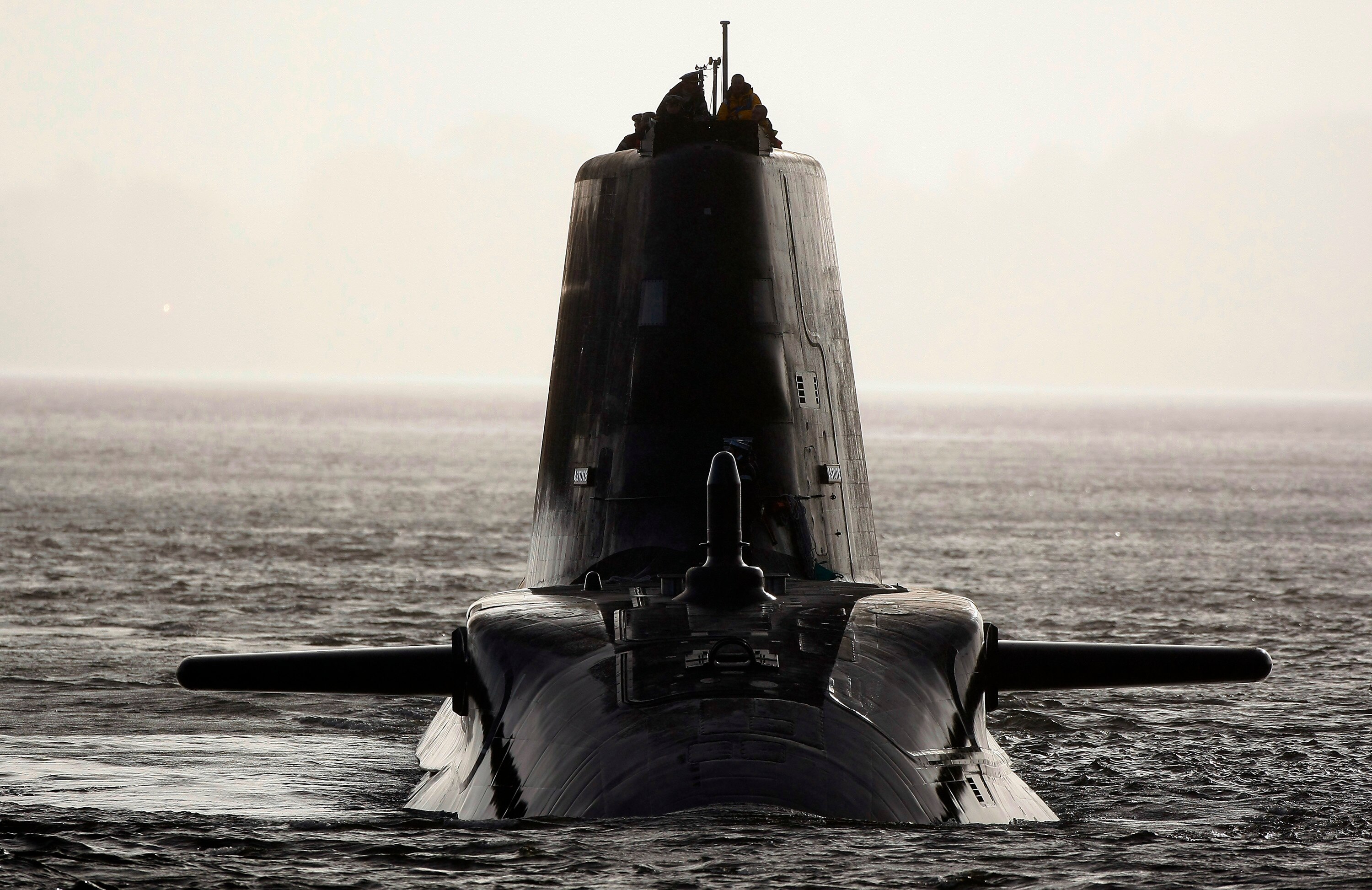 A sleek, modern dark-grey submarine faces the camera in silhouette on the surface of the water.