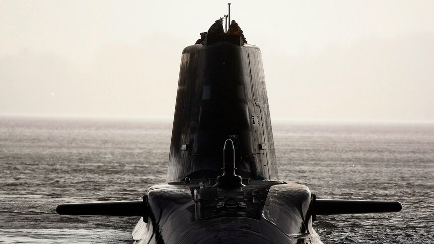 A sleek, modern dark-grey submarine faces the camera in silhouette on the surface of the water.