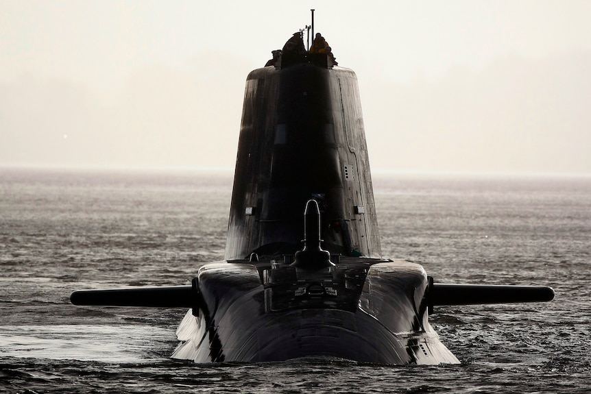 A submarine sails through the water with two crew members in the tower.