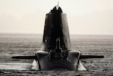 A sleek, modern dark-grey submarine faces the camera in silhouette on the surface of the water.
