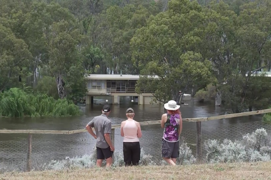 Three people look at a flooded house from a lookout.