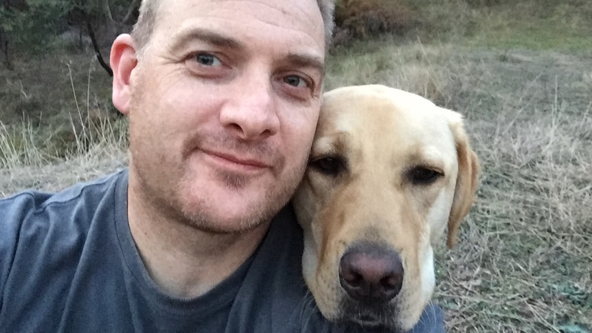 Close up of Rob Atkins in the bush with his assistance dog Jimmy resting its head on Rob's shoulder