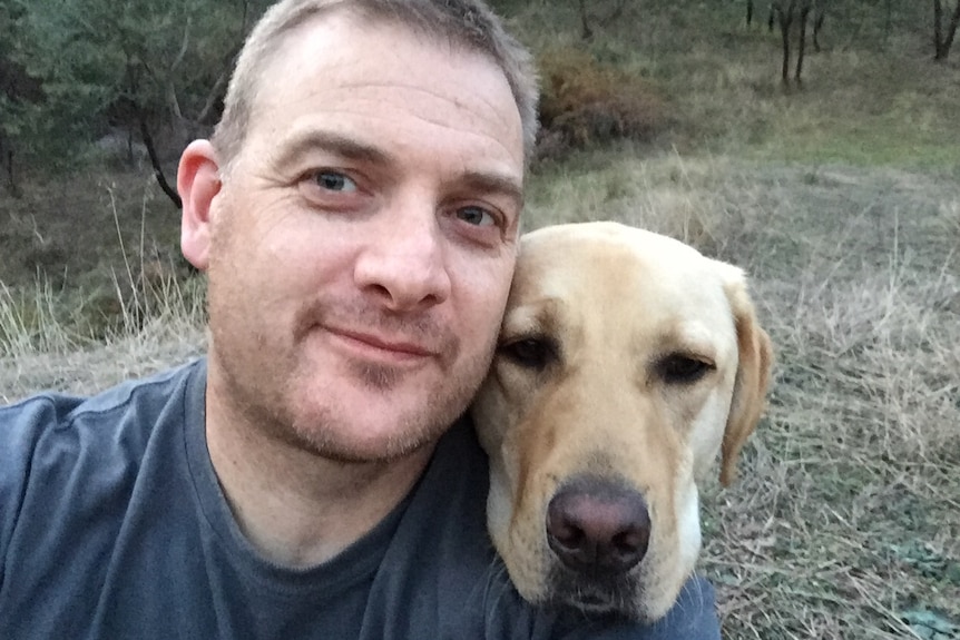 Close up of Rob Atkins in the bush with his assistance dog Jimmy resting its head on Rob's shoulder