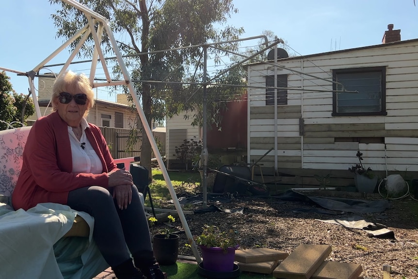 A woman sitting on a swing in the back yard of a house, which is flood-damaged