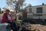 A woman sitting on a swing in the back yard of a house, which is flood-damaged