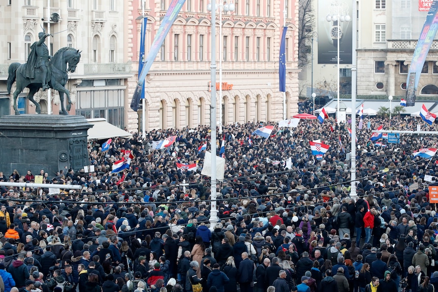 Thousands of people fill a town square holding Croatian flags.
