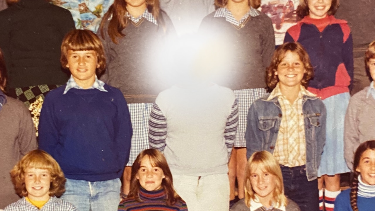 School photo with two boys smiling as they stand in middle row. Student in between them is blurred.