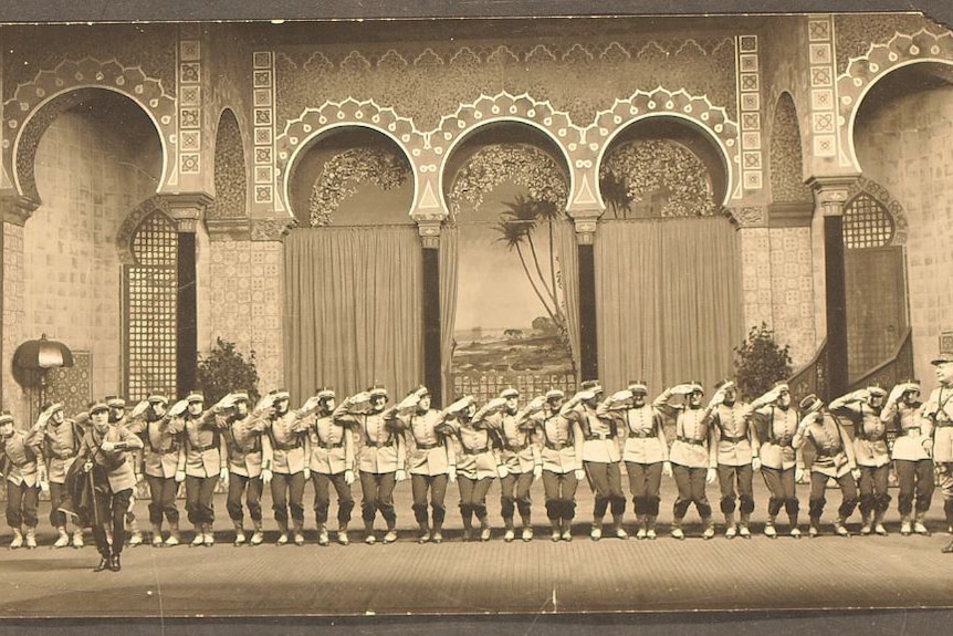 A black and white photo of an old theatre production, a long line of soldiers at attention