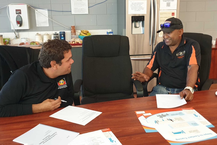 Two Aboriginal men talk at a table.