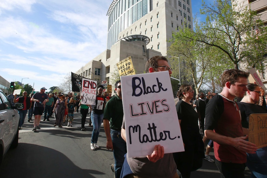 Wide shot of protestors marching down a street with 'Black Lives Matter' signs.