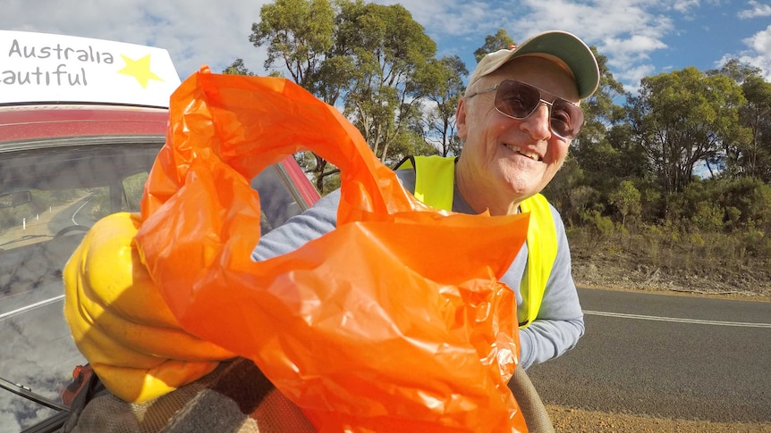 Australia Beautiful volunteer Michael Filby holds up an orange bag of rubbish.