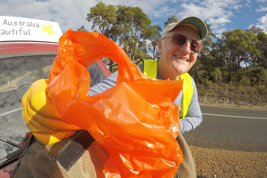 Australia Beautiful volunteer Michael Filby holds up an orange bag of rubbish.