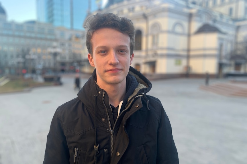 A young man in a black jacket poses in a square in Kyiv.