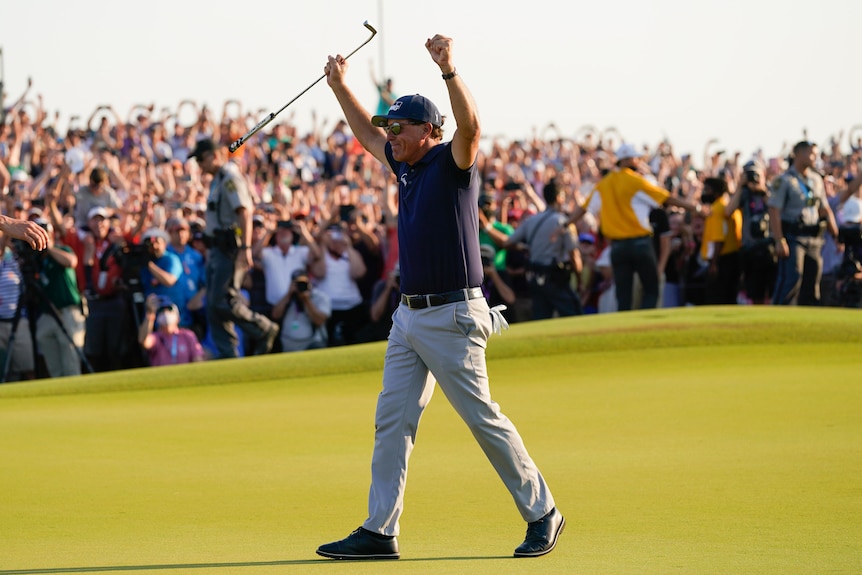 Phil Mickelson holds his hands up in celebration while walking off the green.The crowd behind him is going crazy