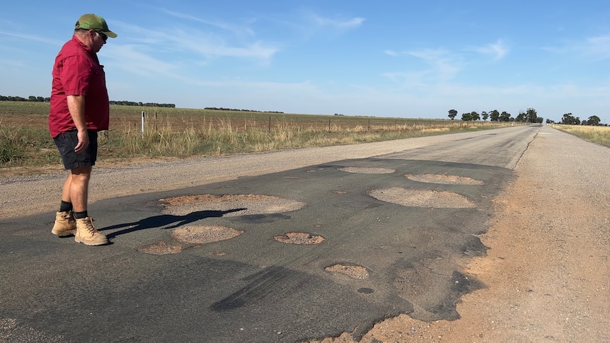 man standing next to road with about eight big holes