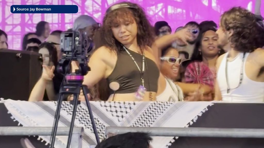 A big crowd of party people dance behind a barrier covered in a Palestinian headscarf