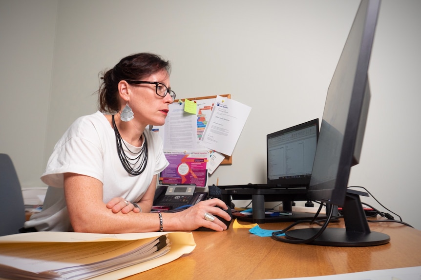 A professional woman in a white shirt sits behind a desk and carefully looks at her computer.