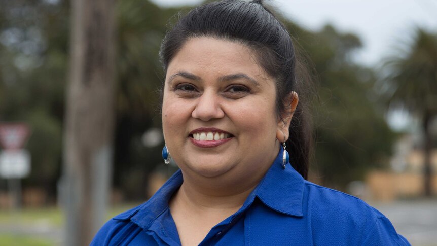 A woman dressed in a blue shirt with matching earrings smiles at the camera