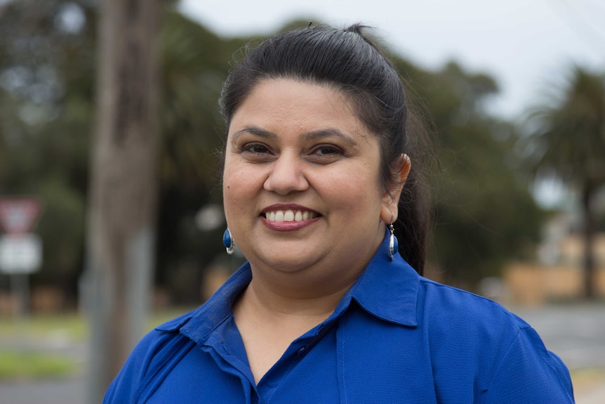 A woman dressed in a blue shirt with matching earrings smiles at the camera