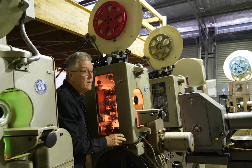 A man stands between a row of vintage cinema projectors.