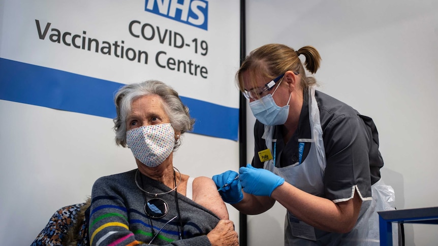 A woman gives a seated woman an injection in her shoulder.