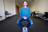 Michael Waite sits smiling on a fold out chair in the middle of his new - and empty - office space for the newspaper.