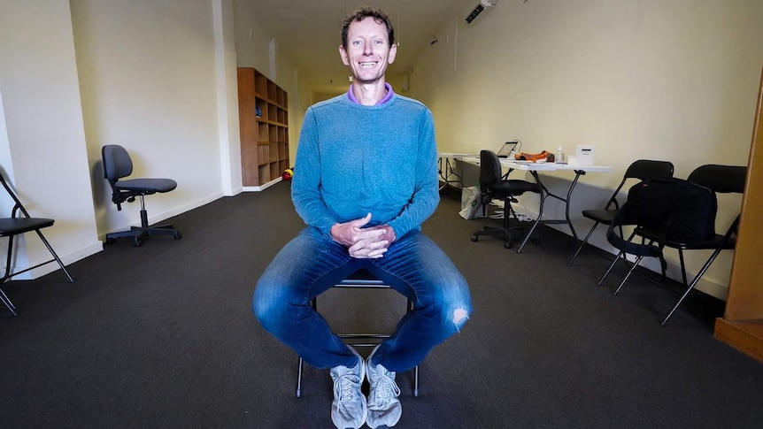 Michael Waite sits smiling on a fold out chair in the middle of his new - and empty - office space for the newspaper.