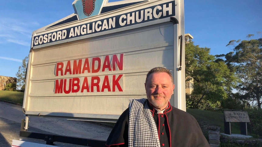 Father Rod Bower stands in front of his church sign.