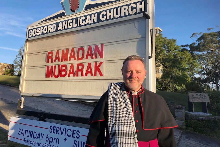 Father Rod Bower stands in front of his church sign.