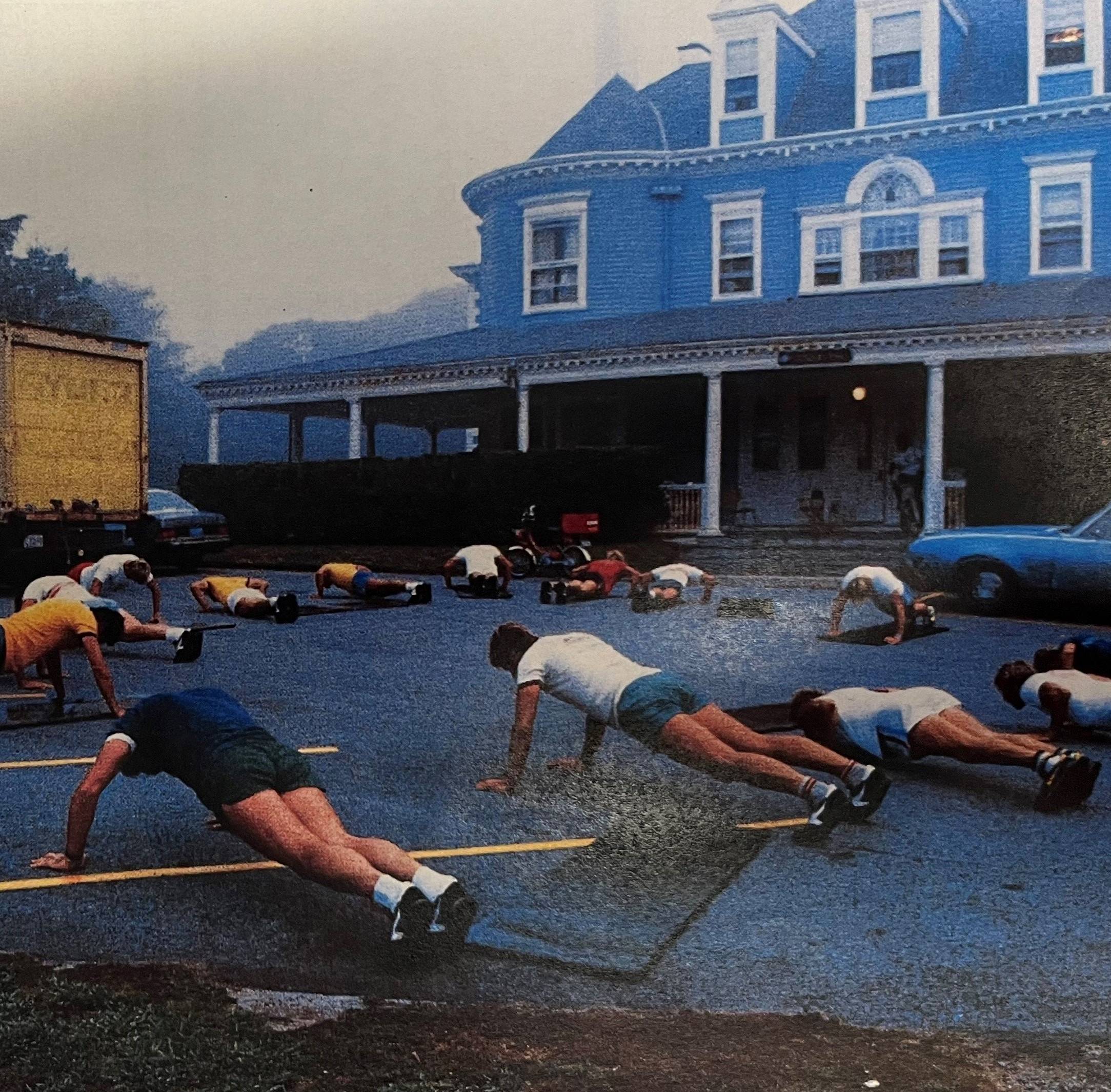 A grainy old photo of several men doing push ups outside a grand old house.