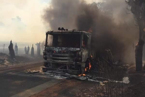 A smouldering fire truck on a rural road with smoke rising around it