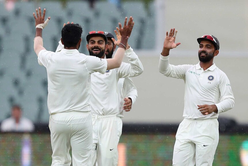 A group of men high five with smiles on their faces