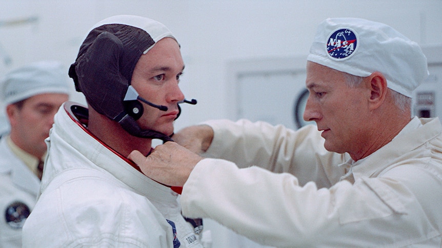 A NASA worker dressed in all white, helping astronaut Buzz Aldrin with the collar of his spacesuit.