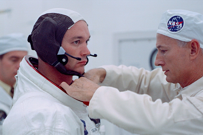 A NASA worker dressed in all white, helping astronaut Buzz Aldrin with the collar of his spacesuit.