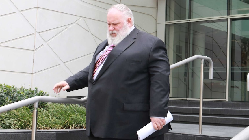 A large man in a white beard wearing a suit walks down the steps outside the Perth District Court.