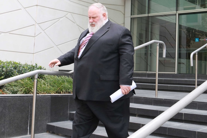 A large man in a white beard wearing a suit walks down the steps outside the Perth District Court.